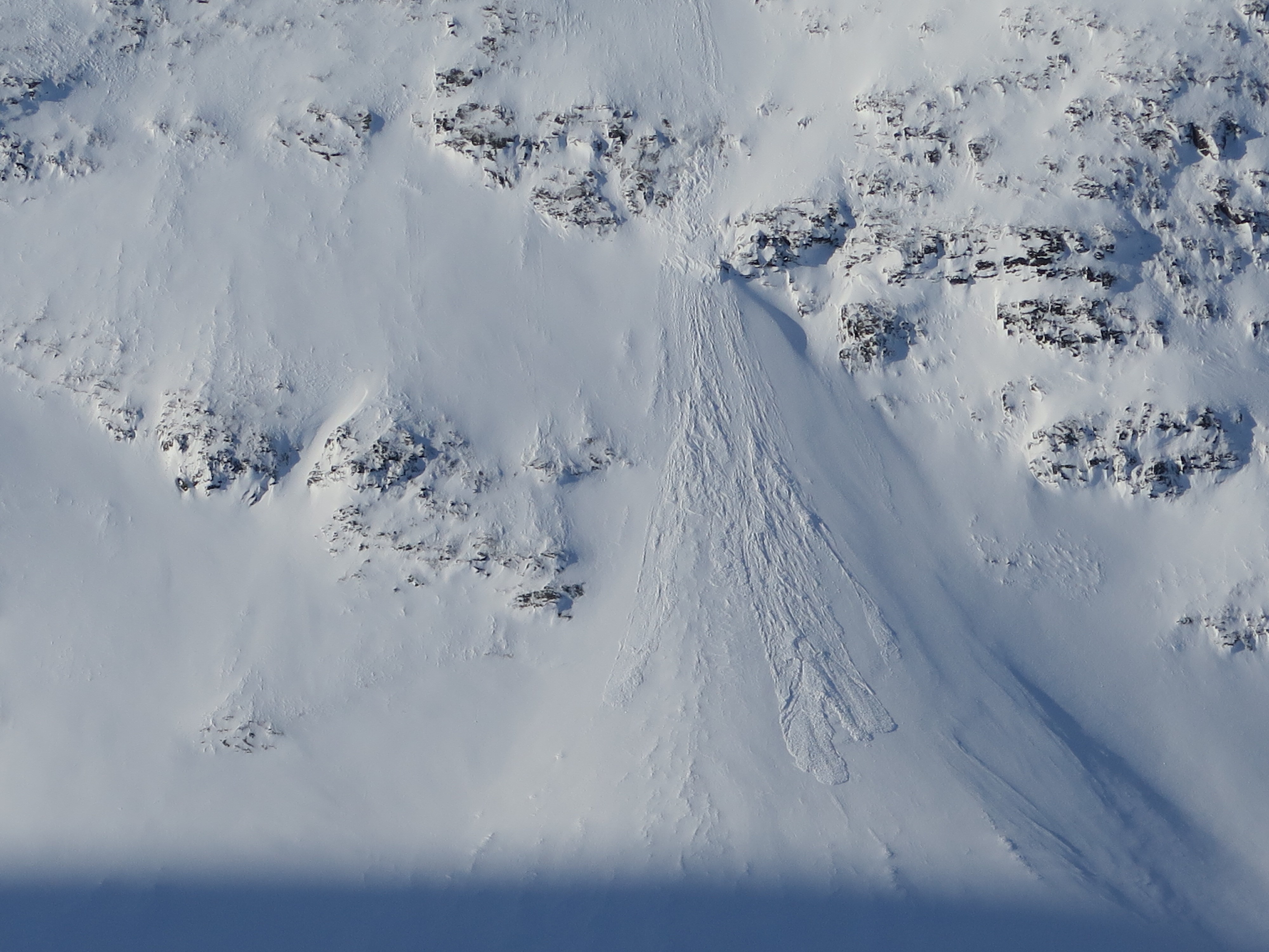 Snötäckt berg och du ser spår av en lavin som utlöst från berget.