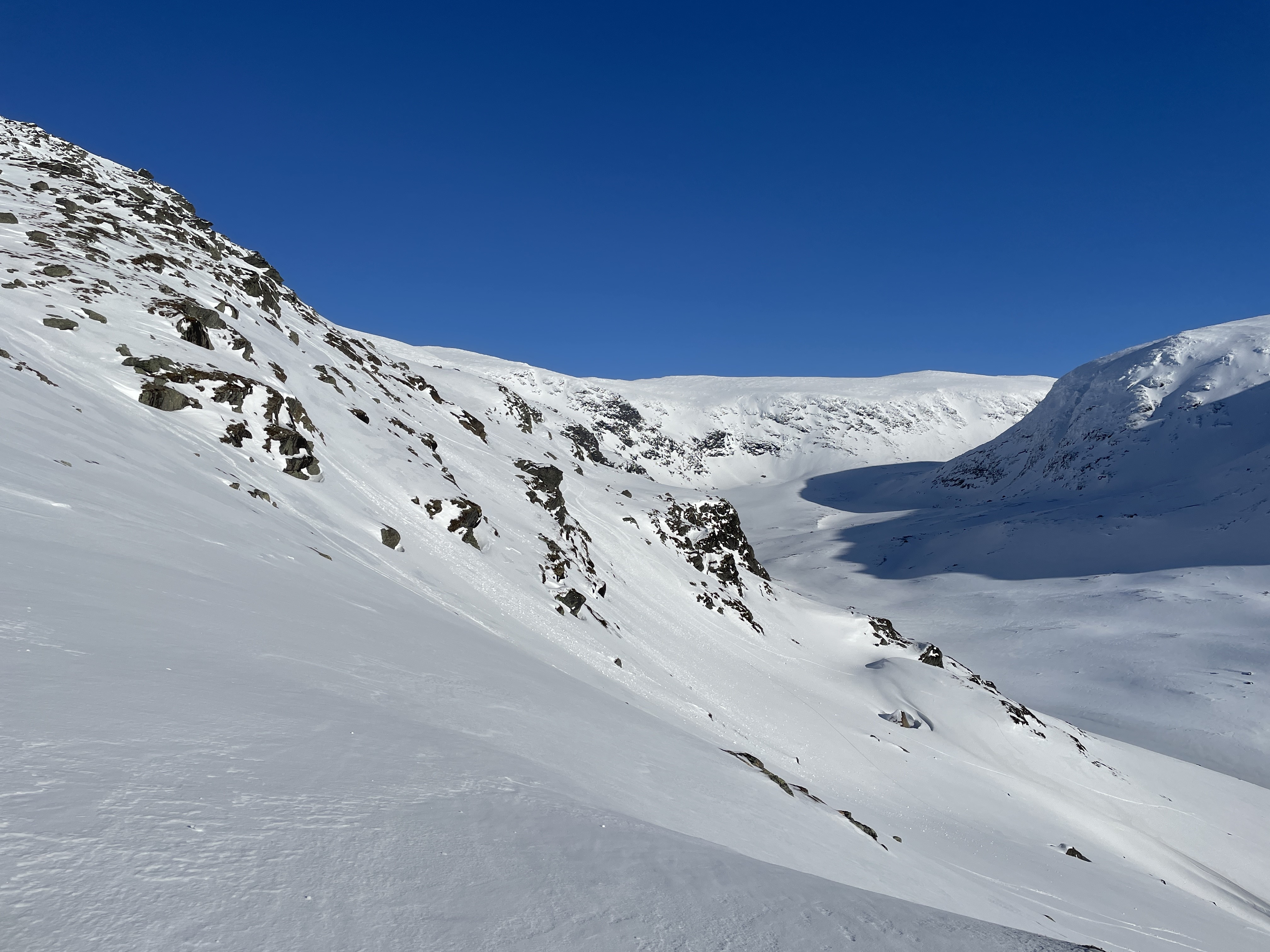 Sluttning av ett snöklätt fjäll med blå himmel i bakgrunden.