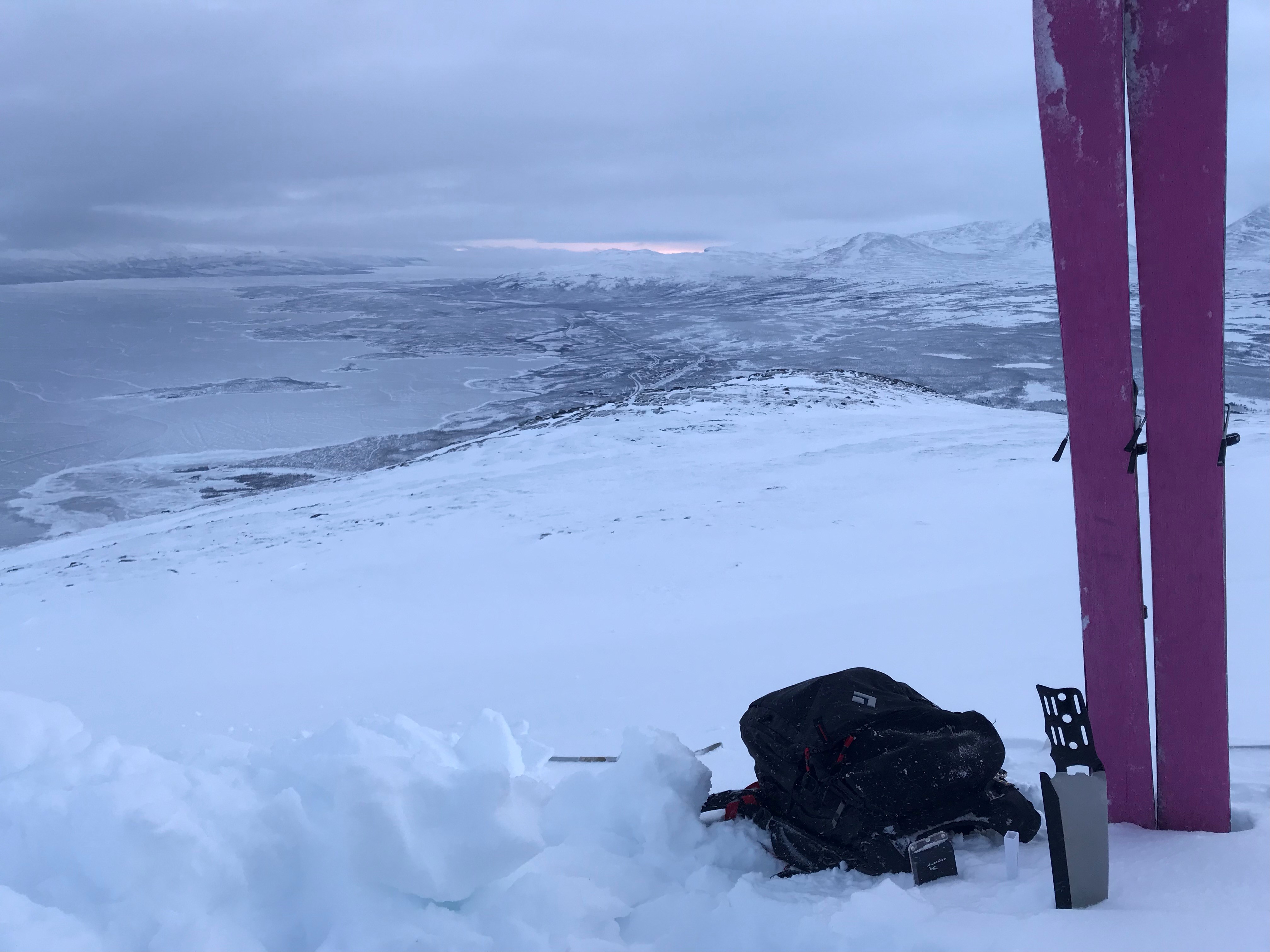 Vy över ett snöklädd dalgång och ett par röda skidor som står nerstuckna i snön i förgrunden.
